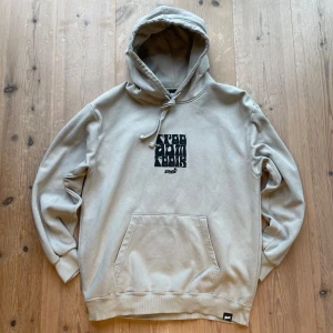 Beigegrå hoodie från Pull&Bear - Säljer en beigegrå hoodie från Pull&Bear med svart grafiskt tryck fram och bak. Hoodien har en klassisk känguruficka och justerbar huva med snöre. Hör av dig vid frågor!