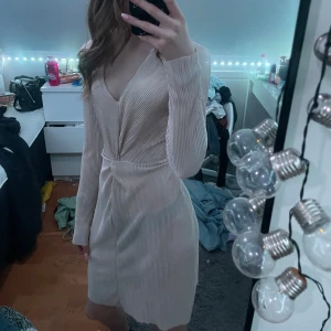 Beige omlottklänning från Gina Tricot - Säljer en elegant beige omlottklänning från Gina Tricot i storlek XS. Klänningen har en v-ringad design och långa ärmar, perfekt för en stilren look. Materialet har en lätt glansig finish som ger en lyxig känsla.