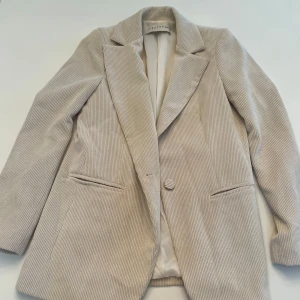 Beige randiga kostym Futur3 - Snygga beige kostymbyxor med diskret randigt mönster. Byxorna har en klassisk rak passform och är perfekta för en stilren look. De är tillverkade i ett mjukt material som ger en bekväm känsla hela dagen.