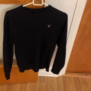 Mörk blå  tröja från Gant - Snygg svart tröja från Gant med rund hals och långärmad design. Perfekt för en stilren look. Diskret logga på bröstet ger en exklusiv touch.