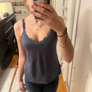 Mörkblå linnetopp med spetsdetaljer - Snygg mörkblå linnetopp med spetsdetaljer längs v-ringningen. Perfekt för en avslappnad stil. Axelbanden är smala och toppen har en figurnära passform.