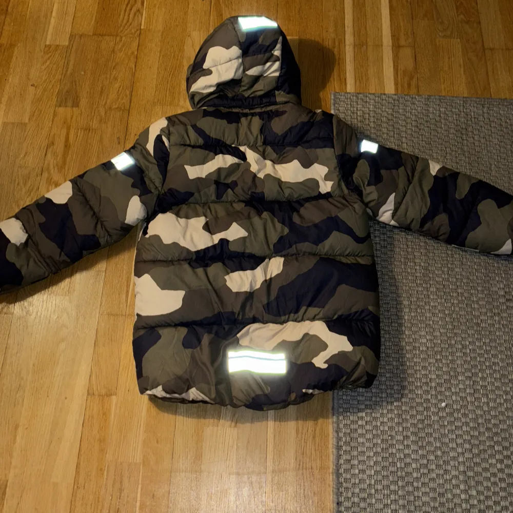 Säljer en cool camouflage pufferjacka från Lindex i storlek 128. Jackan har en huva och praktiska fickor framtill. Den är vattenavvisande och har reflekterande detaljer på ärmarna. Perfekt för höst- och vinterdagar!. Takit.