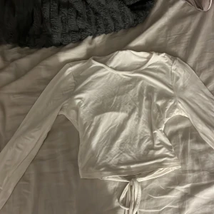 Vit långärmad topp med knyt på ryggen - Säljer en stilren vit långärmad topp med knyt i midjan. Toppen har en rund halsringning. Den är köpt från h&m och är i väldigt bra skick då jag itne användt den så mycket❤️jag har även ett likadant i svart❤️
