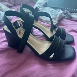 Svarta sandaler med klack - Snygga svarta sandaler med klack och justerbart spänne. Perfekta för en stilren look med sina breda remmar och bekväma passform.