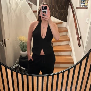 Svart korsett med öppen rygg - Snygg svart korsett med halterneck och öppen rygg. Den har en stilren design med hakknäppning framtill. Perfekt för en kväll ute eller en speciell tillställning.