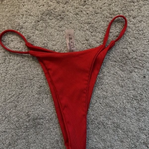 Röd ribbad bikiniunderdel - Snygg röd bikiniunderdel med ribbad textur och smala band. Perfekt för en dag på stranden eller vid poolen. Enkel och stilren design som ger en modern look.  Aldrig använd! 