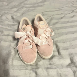 Rosa sneakers från Puma med satinband - Säljer ett par supergulliga rosa sneakers från Puma med unika satinband som snörning. Skorna har en vit sula och en silverfärgad rand på sidan. Perfekta för en stilren och bekväm look.