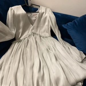 Ljusgrön klänning från H&M - Säljer en elegant vit klänning från H&M med v-ringning och långa ärmar. Klänningen har en fin volangdetalj i midjan och är perfekt för en stilren look. Passar bra till både vardag och speciella tillfällen. Helt ny!