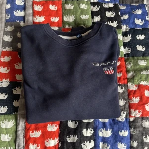 Mörkblå tröja från GANT - Säljer en stilren mörkblå tröja från GANT med broderad logga på bröstet. Tröjan har en klassisk rund halsringning och är tillverkad i ett mjukt material. Perfekt för en avslappnad stil.