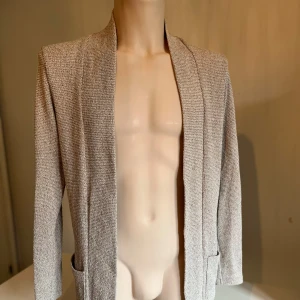 Beige cardigan från Bershka - Snygg beige cardigan från Bershka med en stilren design. Den har långa ärmar och en öppen front utan knappar. Perfekt för en chic och avslappnad look.