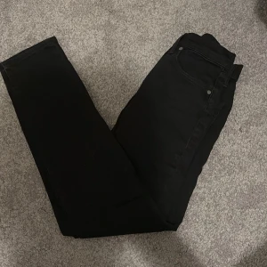 Svarta jeans från Levi's - Snygga svarta jeans från Levi's med en klassisk design. De har en rak passform och är perfekta för en stilren look. Jeansen har fem fickor och en knappgylf.