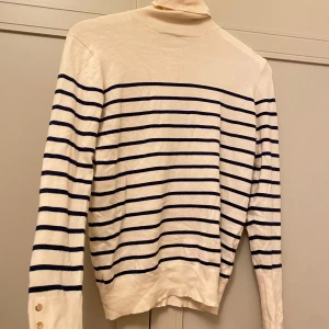 Vit och blå randig polotröja - Säljer en stilren vit polotröja från Zara med blå ränder och guldknappar på ärmen. Tröjan har långa ärmar och en klassisk polokrage. 🤍💙✨