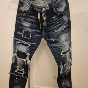 Dsquared2 Jeans *NYA!* - Säljer ett par coola rippade jeans med färgstänk. De har en unik design med slitningar och en dragkedja fram. Perfekta för en avslappnad och trendig look. Passar bra till både vardag och fest! Dsquared2 helt nya jeans. Mått på midja 80cm. 