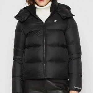 Svart dunjacka från Calvin Klein - Säljer en snygg svart dunjacka/vinterjacka från Calvin Klein. Den har en dragkedja framtill och en mysig huva. Perfekt för kalla vinterdagar och höstpromenader. Jackan är i mycket bra skick och har en stilren design med CK-logga på bröstet💛💛💛 priset kan diskuteras vid seriösa köpare, och jackan kommer självklart tvättas innan den skickas!🤩🤩