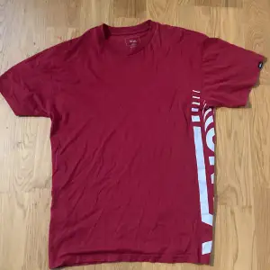 Säljer en snygg röd t-shirt från Vans i storlek medium. Den har ett stort vitt Vans-tryck på sidan som ger en cool look. T-shirten är i bomull och har en klassisk passform. Perfekt för vardagsbruk eller en avslappnad dag ute. 🛹