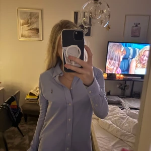 Blå skjorta från Ralph Lauren - Säljer en snygg blå skjorta från Ralph Lauren i storlek S. Skjortan har en klassisk design med knappar och en liten broderad logga på bröstet. Perfekt för både vardag och fest! 💙
