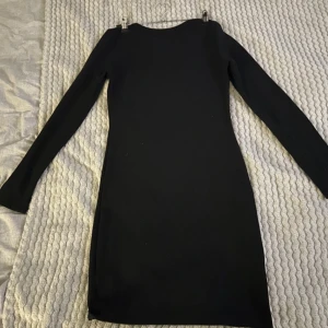 Svart långärmad klänning - Snygg svart långärmad klänning i tight passform. Perfekt för höst och vinter, den är både stilren och bekväm. Klänningen är i ett mjukt material som formar sig fint efter kroppen. Passar både till vardags och festliga tillfällen.