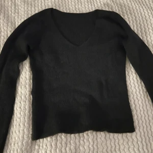 Svart ribbad tröja - Säljer en svart stickad ribbad tröja med v-ringning. Perfekt för både vardag och fest. Tröjan har långa ärmar och är i mycket bra skick. Passar perfekt till höst- och vintergarderoben.