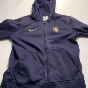 Chealse hoodie från Nike  - Säljer en mörkblå chealse hoodie från Nike i storlek 158 Den har en dragkedja framtill och en snygg guldfärgad chealse logga på bröstet. Perfekt för höst och vår, med en skön passform och fickor framtill. Grym för både träning och vardag! 🏃‍♂️