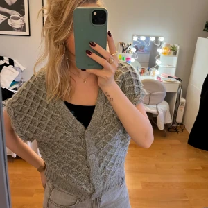 Grå stickad kofta - Säljer en mysig grå stickad kofta med korta ärmar och knappar framtill. Perfekt för lager-på-lager-stil och passar bra till både jeans och kjol. En stilren och bekväm tröja för alla tillfällen.