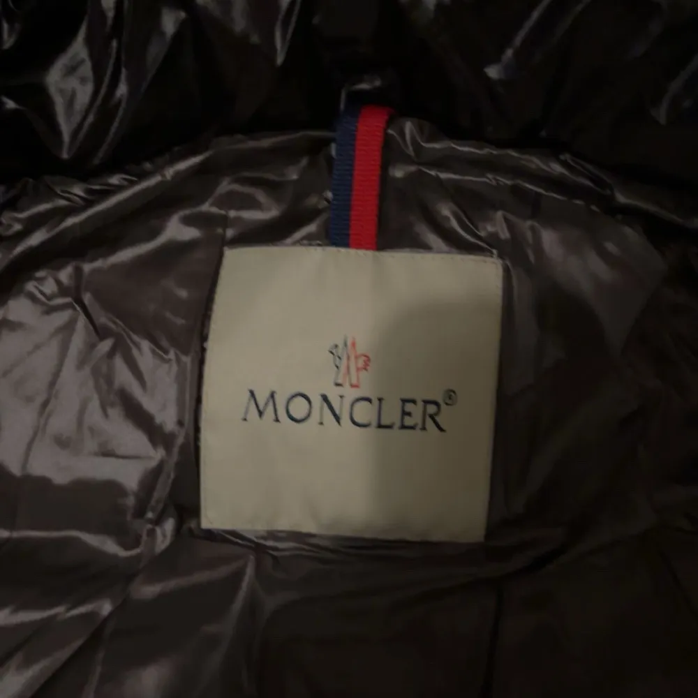 Snygg svart dunjacka från Moncler med glansig finish och dragkedja framtill. Jackan har en klassisk Moncler-logga på ärmen och praktiska fickor med knappar. Perfekt för kyliga dagar.. Jackor.