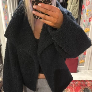 Blå teddyjacka - Mysig svart teddyjacka i mycket bra skick. Perfekt för höst och vinter med sin fluffiga och varma design. Jackan har en oversized passform och långa ärmar, vilket gör den superbekväm och trendig. Den stängs med knappar framtill och har en stor krage 