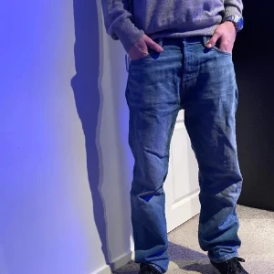 Blåa Weekdays - Säljer ett par klassiska blå jeansbyxor med normal passform. Byxorna har en rak stil och är perfekta för en avslappnad look. De har fickor både fram och bak samt en knapp och dragkedja framtill.