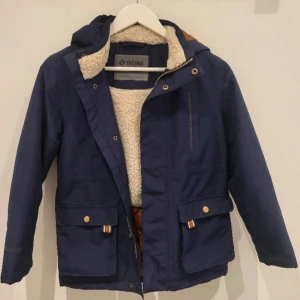 Blå jacka från ZigZag - Säljer en snygg blå jacka från ZigZag i storlek 10 (140-146). Jackan har en mysig fleecefoder och praktiska fickor med knappar. Perfekt för höst och vinter med sin varma och tåliga design. Den har en dragkedja och knappar framtill samt en huva för extra skydd mot väder och vind.