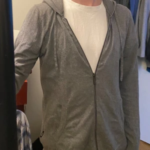 Kashmir zip hoodie - Säljer en gra kashmir&bomull hoodie från strellson i bra skick. Den har dragkedja och en skön huva med snören. Storleken är herr M och materialet är mjukt och bekvämt. Lite stora i armarna men det är modell. Se första bild