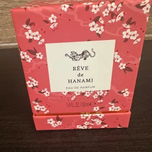 Rêve de Hanami Eau de Parfum från Rituals - Säljer en lyxig parfym, Rêve de Hanami från Rituals. Flaskan är elegant i röd glas med en vit träkork och en guldig etikett. Förpackningen är superfin med rosa och vita blommor. Perfekt för att ge en touch av elegans till din dagliga rutin. Flaskan innehåller 50 ml.