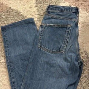 Blå jeansbyxor - Säljer ett par klassiska blå jeans med hög midja och rak passform. Byxorna har fem fickor och stängs med knapp och dragkedja. Perfekta för en avslappnad stil.