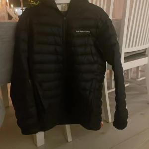 Svart dunjacka från Peak Performance - Säljer en svart dunjacka från Peak Performance i bra skick. Jackan har en dragkedja framtill och är perfekt för höst och vinter. Den är långärmad och quiltad för extra värme. Det finns ett litet hål (se bild) som är lagat så det märks knappt. Perfekt för dig som vill ha en stilren och varm jacka! 🖤