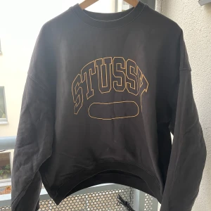 Svart sweatshirt från Stussy - Säljer en svart sweatshirt från Stussy i mycket bra skick. Den har ett stort tryck med Stussy-loggan i gult på framsidan. Tröjan är perfekt för en avslappnad stil och passar bra till både jeans och joggers. Den är långärmad och har en normal passform. Perfekt för höst och vår!