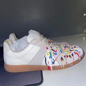 MAISON margelas GATs - Tjena, säljer nu ett par eftertraktade MAISON margela GATs. Sneakers med ett färgglatt stänkmönster i rött, blått, gult och svart på en vit bas. Skorna har en brun sula och snörning. Skick är 9/10 knappt använda. Endast dustbag medföljer. Perfekta för att ge din outfit en kreativ touch. Om funderingar hör av dig till mig. ✌🏻☺️
