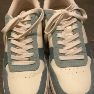 Vit och blå sneakers - Säljer ett par snygga sneakers i vitt och blått. De har en klassisk design med snörning och är i mycket bra skick. Perfekta för både vardag och lite mer avslappnade tillfällen. Storlek herr 42. Använda 1 gång 