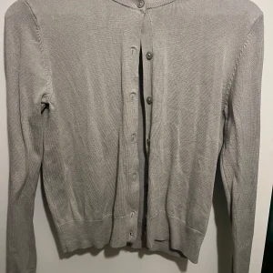 Grå kofta från H&M - Säljer en stilren grå/olivgrön/beige kofta från H&M i storlek S. Den har långa ärmar och knappar framtill. Supermjuk och bekväm att ha på sig! Knappt använd, så superbra skick!💕😌