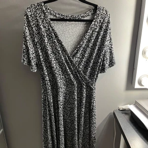 Svartvit blommig klänning från Indiska - Säljer en svartvit klänning från Indiska med blommigt mönster. Klänningen har en omlott-design och korta ärmar. Den går till knäna för mig som är 164. Helt oanvänd, är uppenbarligen inget fan av klänningar då den bara hängt i garderoben! 