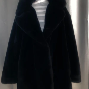Svart pälsjacka - Elegant svart pälsjacka med långärmad design. Perfekt för kyliga dagar med sin mjuka och lyxiga känsla. Jackan har en klassisk stil och är fodrad för extra värme.