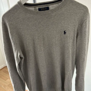 Grå tröja från Polo Ralph Lauren - Säljer en stilren grå tröja från Polo Ralph Lauren med det klassiska logotypbroderiet på bröstet. Tröjan har långa ärmar och en rund halsringning, perfekt för en avslappnad men snygg look.