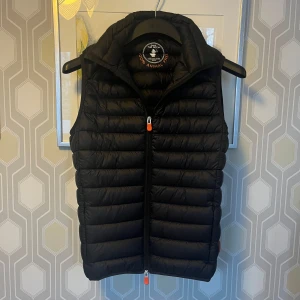  Save The Duck dunväst - Säljer en svart dunväst från Save The Duck i storlek S. Västen är quiltad och har en dragkedja framtill.  Perfekt till lager på lager nu under kyligare dagar!