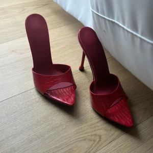 Röda klackskor med spetsig tå - Snygga röda klackskor med spetsig tå och hög klack. Skorna har en elegant design med ett krokodilmönster som ger en lyxig känsla.