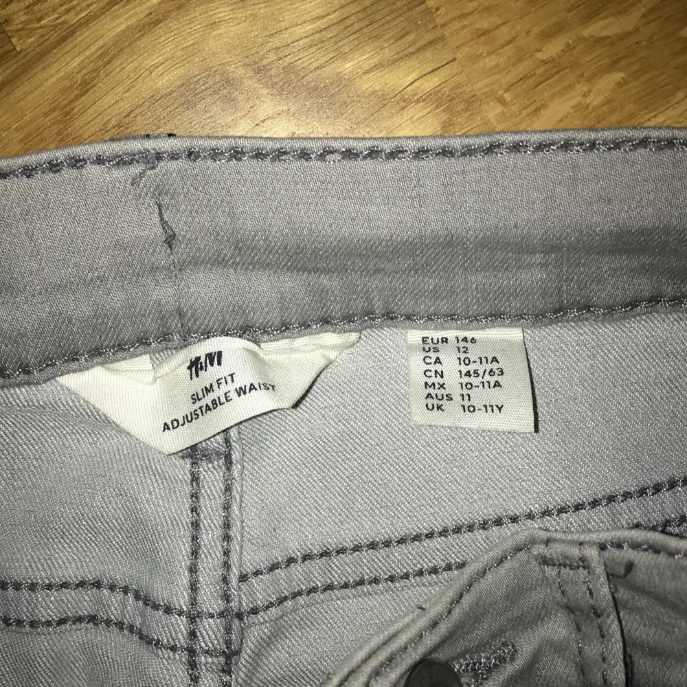 Säljer ett par grå slim fit byxor från H&M med justerbar midja. Perfekta för en stilren look och bekväma att bära. Passar för barn i åldern 10-11 år.. Jeans & Byxor.