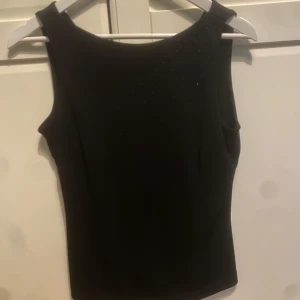 Svart blus från Mexx - Snygg svart blus från Mexx i ett elegant och stilrent snitt. Den är ärmlös och har små glittriga detaljer på framsidan som ger en extra touch. Perfekt för festliga tillfällen eller en utekväll. Blusen är i mycket bra skick och passar bra till både höst och sommar🥰