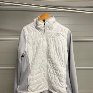 Vit fleecejacka från The North Face - Säljer en snygg vit fleecejacka från The North Face i mycket bra skick. Jackan har en dragkedja framtill och är långärmad med gråa ärmar. Perfekt för kyliga höst- och vårdagar. Den är både bekväm och stilren, idealisk för vardagsbruk eller lättare utomhusaktiviteter. Säljes i befintligt skick. Storlek: M/S
