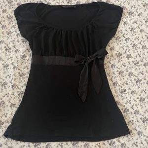 Svart topp med rosett - Babydoll top med en dekorativ rosett i midjan. Perfekt för en gullig look. 👀🎀