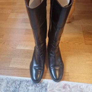 Svarta stövlar i skinn - Snygga svarta stövlar med vinröd innerkant. Gjorda av skinn med varmt foder på insidan. De har en klassisk design med spetsig tå och är perfekta för höst- och vintergarderoben. Nyskick, aldrig använda. 