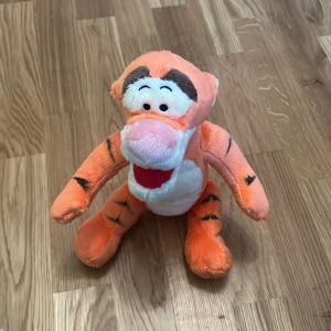 Tigger gosedjur från Disney - Säljer ett mjukt och gosigt Tigger gosedjur från Disney. Det är orange med svarta ränder och har en vit mage. Perfekt för alla som älskar Nalle Puh och hans vänner! 🐯