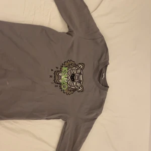 Grå tröja med tigertryck - Snygg grå tröja med ett coolt tigertryck i svart och grönt på framsidan. Tröjan har långa ärmar och en rund halsringning. Perfekt för en avslappnad stil.