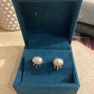 Pärlörhängen från Léc. - Eleganta pärlörhängen från Léc. I en stilren design. De har en vit keshi pärla i mitten med blixtar gjorda av 925 sterling silver och ovan på det är dom rodium platterade som gör att det inte tappar färg eller blir repiga. Endast använda fåtal gånger och är i nyskick. Dom är ungefär en centimeter stora. Perfekta för att lyfta vilken outfit som helst. Nypris ca 1100kr