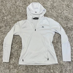 J.Lindeberg halfzip - Säljer en stilren vit hoodie från J.Lindeberg. Den har en dragkedja framtill och en bekväm huva. Perfekt för både vardag och träning. Den är i mycket bra skick och passar till alla säsonger.